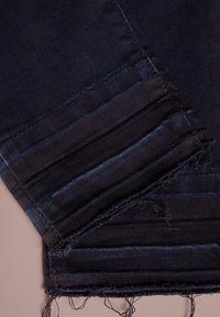 Close-up van opgevouwen donkerblauwe denim jeans met zichtbare stiksel en rafelige randen op een lichte ondergrond.