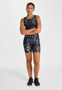 Svart och mörkgrå sportig outfit med en figurnära design, med ett vågmönster och rund halsringning, kombinerad med svarta träningsskor.