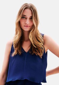 Top sin mangas azul marino con diseño de escote en V, textura suave y una silueta fluida que cae suavemente en el dobladillo.