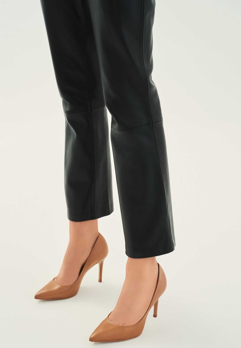 Fekete bőrnadrág egyenes szabással, párosítva hegyes orrú, sima textúrájú bézs magassarkú cipővel.