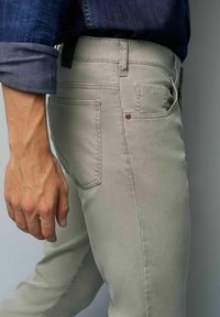 Hellgraue Stretch-Chinos in schlanker Passform, mit Gesäßtaschen, dezenten Nähte-Details und einem dunklen Etikett am Bund.