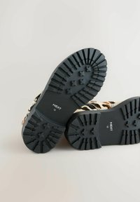 Talpa din cauciuc negru cu un model de dantela, având brandingul "NEXT" și mărimea "12". Designul include un model de imprimeu cu animal.