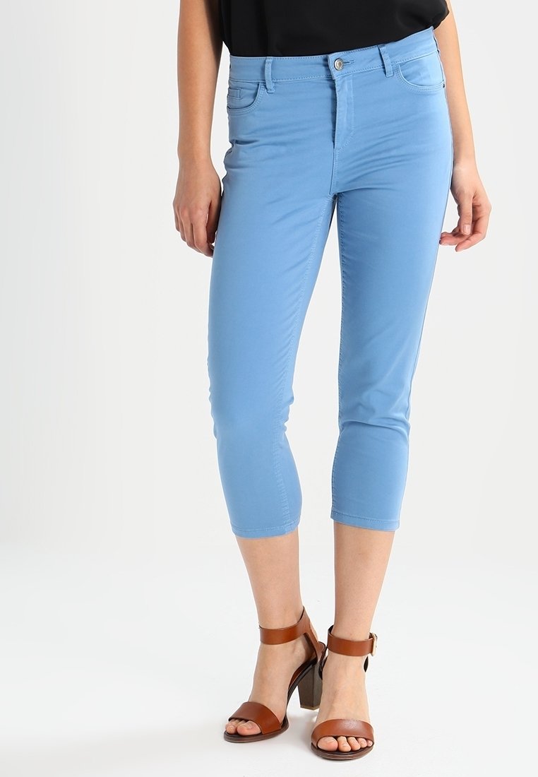 Light blue capri pants made of cotton blend, featuring a fitted design with front pockets and a mid-rise waist. Worn with brown heeled sandals.