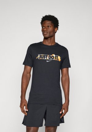 Sort bomulds T-shirt med "JUST DO IT" grafik i gul og hvid, sammen med et Nike-logo, parret med sorte sportshorts.