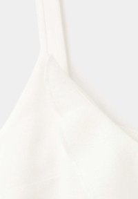 Gros plan d’un vêtement blanc sans manches montrant une bretelle étroite et une texture de tissu douce.