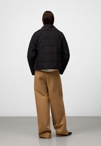 Giacca a puffo nera cropped con un design trapuntato, abbinata a pantaloni beige a gamba larga. Texture liscia e design del colletto semplice.