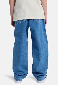 Light blue denim jeans with a loose fit, featuring back pockets and a slightly tapered leg with cuffs resting on white sneakers.