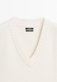 V-hals sweater i off-white, lavet af 100% uld. Har ribbet krave og kant, glat tekstur og mærke indeni halsudskæringen.