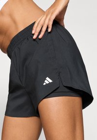 Schwarze Sportshorts mit elastischem Bund, seitlichen Schlitzen und weißem Logo am linken Bein. Glatte Textur, leichter Stoff.