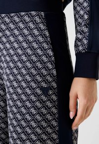 Marineblauwe joggers met een patroon van witte diamanten. Voorzien van een logopatch en contrasterende zijkanten in effen marineblauwe stof. Gladde textuur.