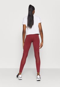 Vinröda leggings med meshpaneler, figurnära design, hög midja och sömdetaljer. Kombineras med en vit croppad t-shirt och svarta sneakers.