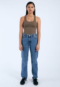 Top in cotone marrone a coste, jeans in denim blu a vita alta, di vestibilità comoda, con chiusura a zip e bottone, abbinato a sneaker nere in suede.