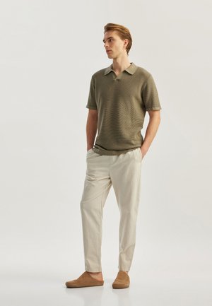 Polo a maniche corte verde oliva con motivo testurizzato, pantaloni su misura color crema e scarpe slip-on marrone chiaro.
