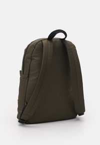 Zaino verde oliva realizzato in tessuto liscio e resistente, con schienale imbottito, spallacci regolabili e maniglia superiore. Tasca laterale discretamente integrata.