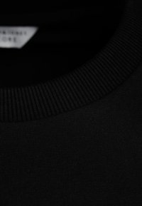Primer plano de una camiseta de algodón negra, con un cuello redondo acanalado y una textura de tela suave, sin patrones ni logotipos visibles.