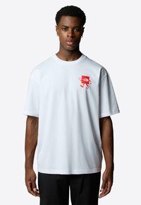 Bílý bavlněný tričko s červeným logem grafiky na levém hrudníku. Krátké rukávy, volný střih, kulatý výstřih. Jednoduchý design, bez vzorů.