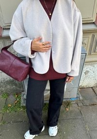 Jasnoszara, oversize'owa kurtka, burgundowy sweter z prążkami, czarne spodnie i białe sneakersy. Dodatki to burgundowa torba i pierścionki.