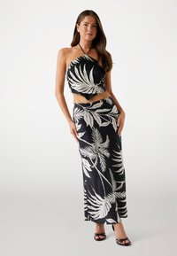 Costum din două piese cu imprimeu floral alb-negru, având un top scurt cu gât halter și o fustă lungă, fluidă, cu o textură netedă.