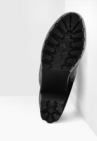 Czarny sneaker z rowkowaną gumową podeszwą, charakteryzujący się unikalnym wzorem bieżnika i gładką teksturą w górnej części.