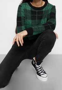 Pull en maille à carreaux verts et noirs avec encolure ras-du-cou, poignets côtelés noirs, associé à un jean skinny noir et des baskets montantes noires.