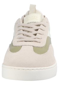 Beige suede sneaker featuring a green rubber accent, white leather details, and round toe design with flat laces. Textured upper and rounded sole.
