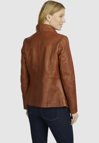 Giacca di pelle marrone con un design strutturato, caratterizzata da un colletto rialzato e una trama liscia, abbinata a jeans scuri.
