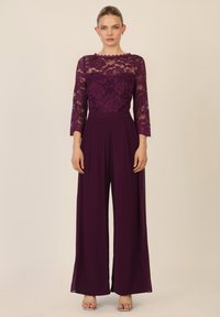 Jumpsuit prugna con un corpetto in pizzo floreale e maniche a tre quarti, caratterizzato da pantaloni larghi e una vita aderente. Tacchi a striscia argento.