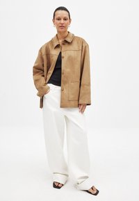 Kerge pruun nahkjakk nupuvajutusega, suure kraega ja kontrastse õmblusega. Ühendatud valgete laia säärega pükstega ja mustade sandaalidega.