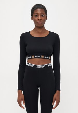 Vrouw draagt een zwarte lange mouwen crop top en leggings met Moschino merk-elastieken met teddybeer motieven.