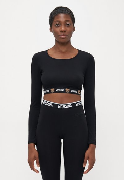 Donna che indossa un crop top lungo nero e leggings con bande elastiche marchiate Moschino, decorate con motivi di orsetti.