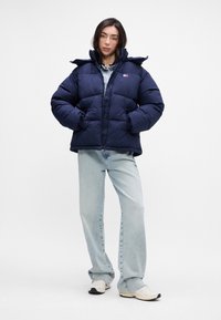 Ναυτικό φορμάκι με επένδυση, ψηλό γιακά και κλείσιμο με φερμουάρ, διαθέτει πλευρικές τσέπες και λογότυπο. Συνδυάζεται με ανοιχτό μπλε τζιν και αθλητικά παπούτσια.