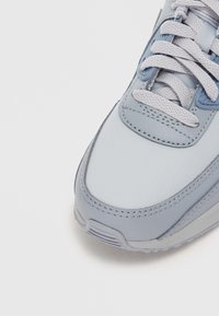 Lys blå joggesko med glatt skinnoverdel, teksturerte detaljer, runde lisser og en gummisåle med diskret mønster.