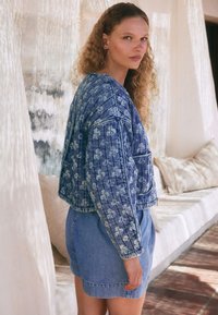 Denimjakke med et blomstermønster i blå nuancer, kort design med ribbede manchetter, kombineret med en matchende denimnederdel.