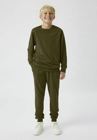 Felpa verde oliva e pantaloni jogger realizzati in tessuto morbido, caratterizzati da una vestibilità comoda e polsini a costine, abbinati a sneaker bianche.