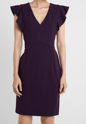 Ærmeløs mørkelilla kjole med dyb V-hals, tilpasset talje og flæse detaljer ved skuldrene båret af en stående person.