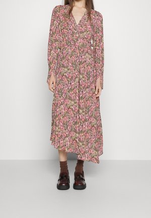 Woman wearing a long-sleeve, pink floral print wrap dress with brown socks and dark brown loafers standing against a plain background.