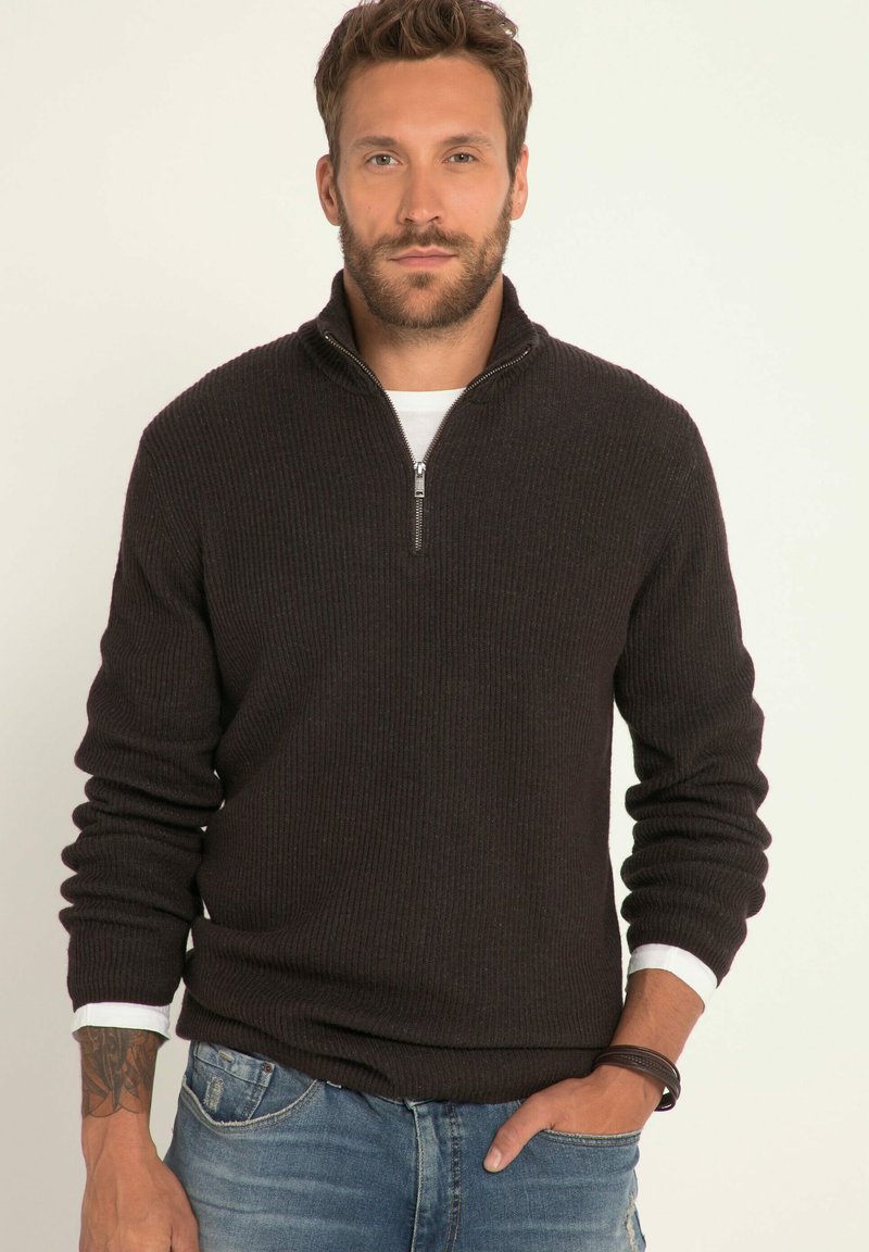 Schwarzer, gerippter Reißverschluss-Pullover mit langen Ärmeln, ausgestattet mit einem weißen Innenkragen und getragen über blauen Jeans. Einfaches, strukturiertes Design.