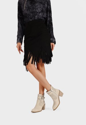 Gonna di suede nera con orlo sfrangiato, abbinata a stivali alla caviglia beige con dettagli a intaglio e tacco impilato.