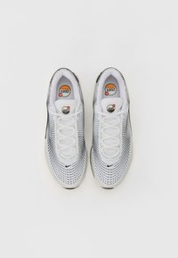 Baltijas baltas un melnas sporta kurpes ar perforētu tīklu augšdaļu, apaļu purngalu, šņorēm un redzamu Air Max zīmolu uz mēles un zoles.