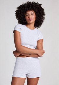 Lys grå kortermet bomullstopp og matchende shorts med knappedetaljer. Myk tekstur, figurnær design og en enkel, minimalistisk stil.