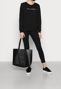 Czarna bluza z haftem "Tommy Hilfiger", czarne dopasowane spodnie i czarna skórzana torba na ramię. Czarne sneakersy z białą podeszwą.