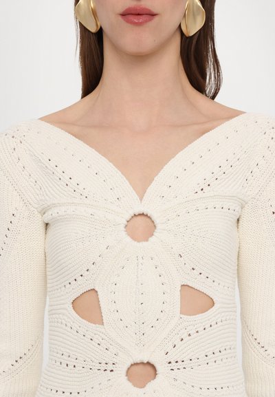Knit white sweater featuring a deep V-neck, cut-out circular details, and textured patterns along the sleeves and body.