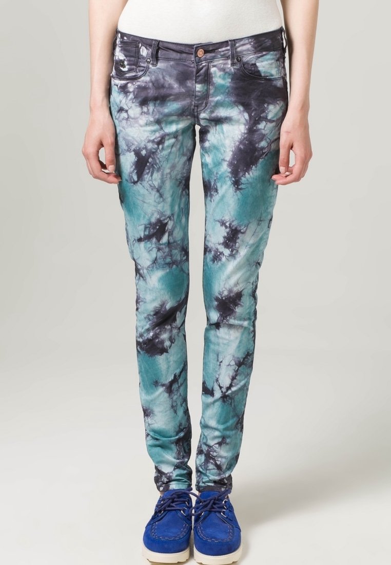 Jean tie-dye en teal et noir. Coupe slim avec poches avant et quincaillerie en métal. Associé à des chaussures bleues pour le contraste.