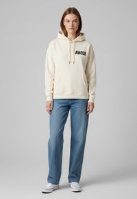 Felpa crema con la scritta "AMOUR" in nero, tasca a marsupio e cappuccio con cordino. Abbinata a jeans azzurri chiari e sneakers bianche.