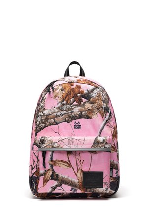 Sac à dos avec fond rose et motif camouflage feuilles et branches marron, poche avant zippée et boucle de poignée noire sur le dessus.