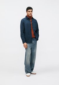 Tumesinine nööbitav jakk roostetoonilise kaelusega, mille juurde kuuluvad laia säärega helesinised teksad ja valged tossud pruunide talladega.