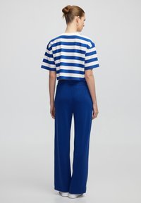 Camiseta blanca y azul a rayas, recortada y de manga corta, combinada con pantalones azules holgados, ambos fabricados en un tejido suave y ligero.