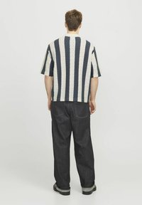 Camicetta a maniche corte a righe blu navy e crema, tessuto testurizzato con motivo a zigzag, abbinata a pantaloni in denim scuro, mostrando una vestibilità rilassata.