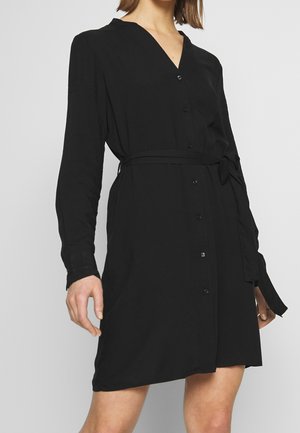 Robe noire boutonnée avec col en V, manches longues, taille ceinturée, texture douce et tissu lisse. Présente des boutons semblables à des perles sur le devant.