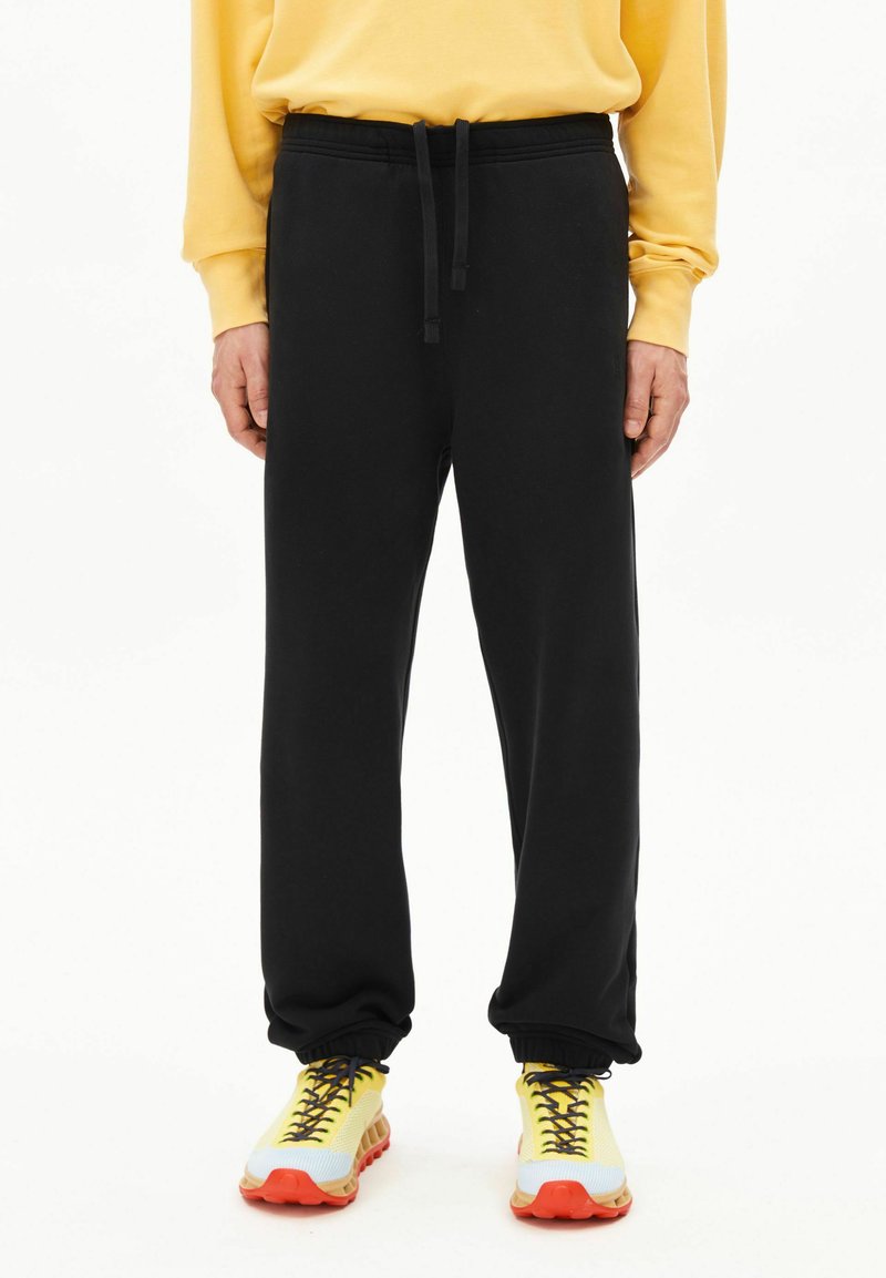 Zwarte joggingbroek met een tailleband met trekkoord en elastische boorden, gemaakt van zacht materiaal, gecombineerd met felgele sneakers.